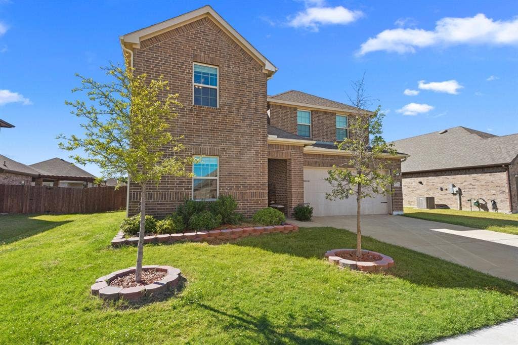 Brick exterior with multi-pane windows, attached garage, concrete driveway, and landscaped front yard with decorative brick edging