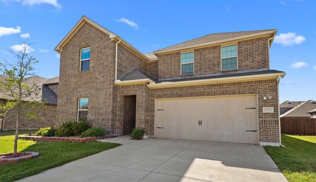 Two-story brick exterior with an attached two-car garage, concrete driveway, and front landscaping