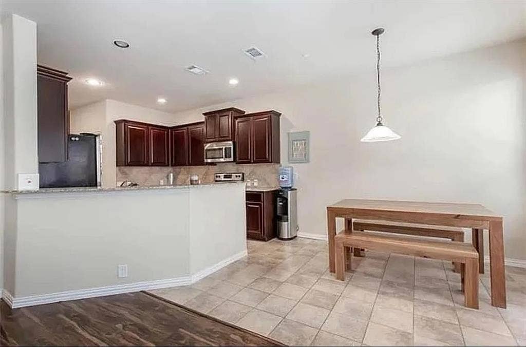 Kitchen featuring light stone countertops, pendant lighting, black refrigerator, kitchen peninsula, and dark brown cabinets