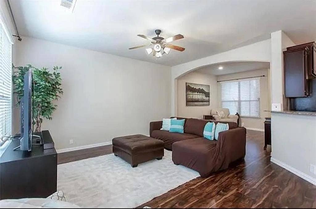 Living room with dark wood-type flooring, ceiling fan, and a wealth of natural light