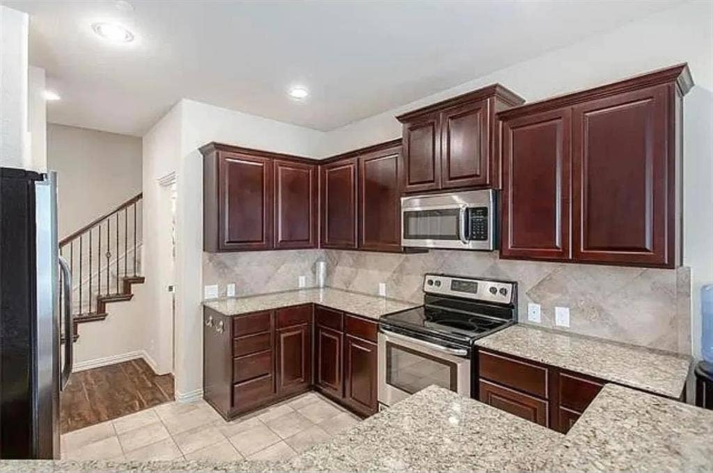 Kitchen featuring light tile patterned floors, backsplash, light stone countertops, and stainless steel appliances