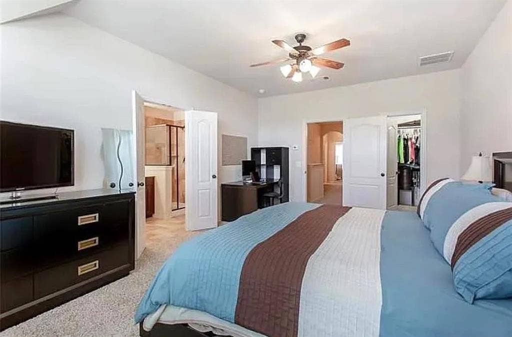 Carpeted bedroom featuring a spacious closet, a closet, ceiling fan, and ensuite bath