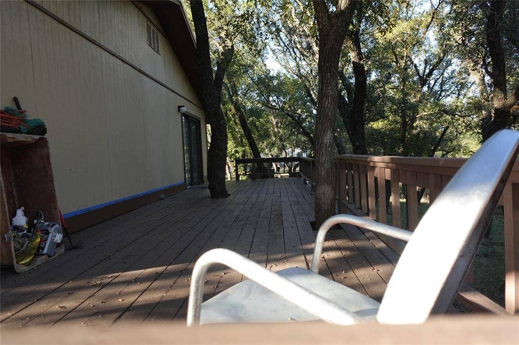 Expansive wood deck with a built-in railing, surrounded by mature trees, and featuring a sliding glass door entry to the property