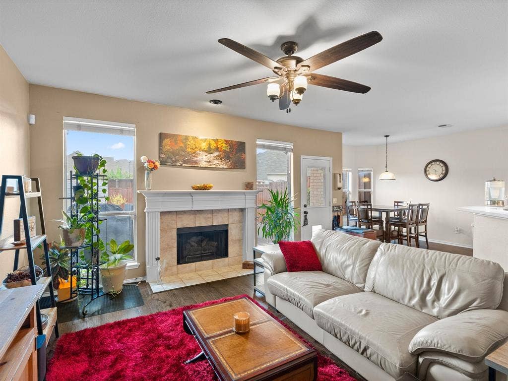 3303 Felicia Court, McKinney, TX 75070 Fireplace featuring a white mantel and tile surround, wood-finish flooring, and a ceiling fan with integrated lighting