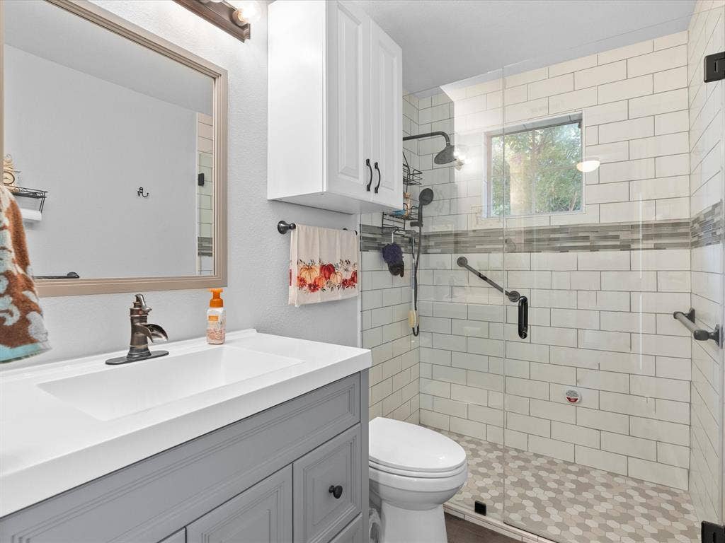 3303 Felicia Court, McKinney, TX 75070 Bathroom featuring a gray vanity with a rectangular sink, wall-mounted cabinet, subway-tiled walk-in shower with a glass panel, and hexagon floor tile