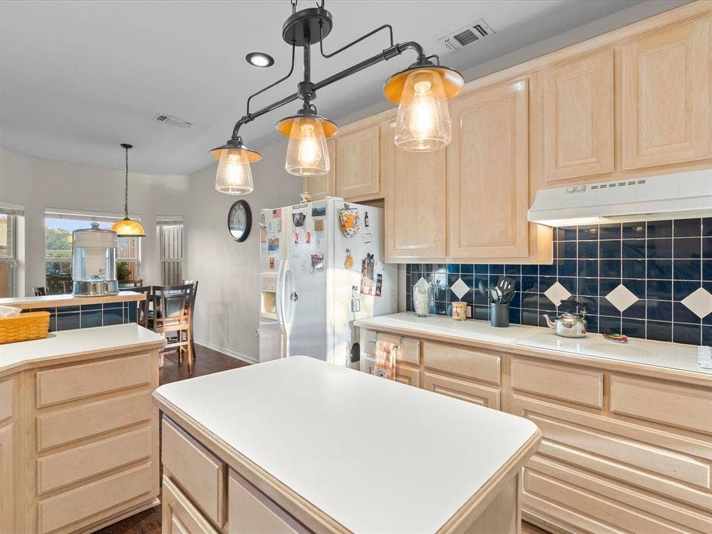 3303 Felicia Court, McKinney, TX 75070 Kitchen featuring light-finish cabinetry, a center island with a solid surface countertop, contrasting dark tile backsplash with diamond accents, and a tiered industrial-style hanging light fixture