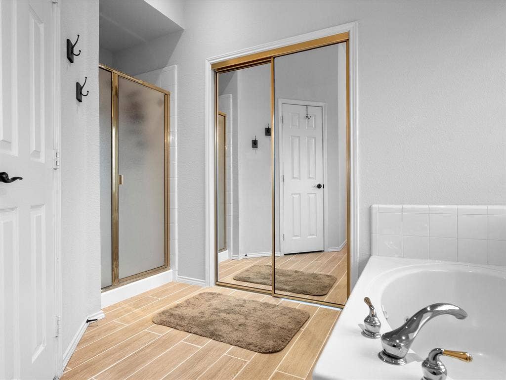 3303 Felicia Court, McKinney, TX 75070 Bathroom featuring wood-finish tile flooring, a soaking tub with polished chrome fixtures, a glass-enclosed shower, and sliding mirrored closet doors