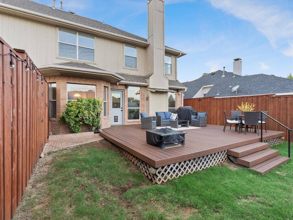 3303 Felicia Court, McKinney, TX 75070 Rear exterior featuring an elevated composite deck with integrated stair access, a wood-slat privacy fence, brick chimney, and multi-pane windows