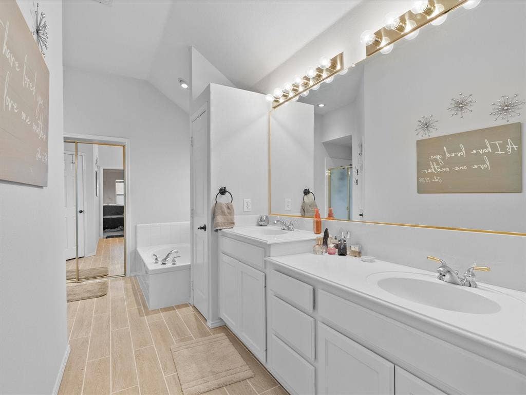 3303 Felicia Court, McKinney, TX 75070 Dual-sink vanity with white cabinetry and countertop, wall-to-wall mirror, integrated light bar, tiled flooring, and built-in soaking tub