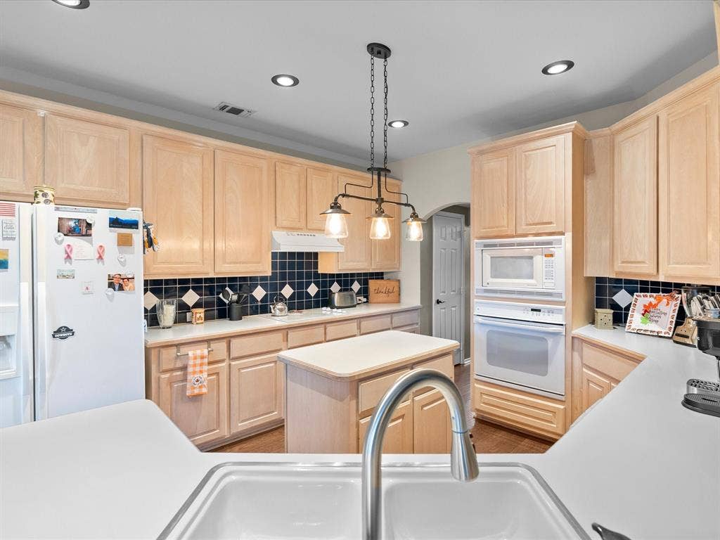 3303 Felicia Court, McKinney, TX 75070 Kitchen featuring light wood cabinetry, white countertops, a center island, dual-basin sink with a gooseneck faucet, and a black tile backsplash