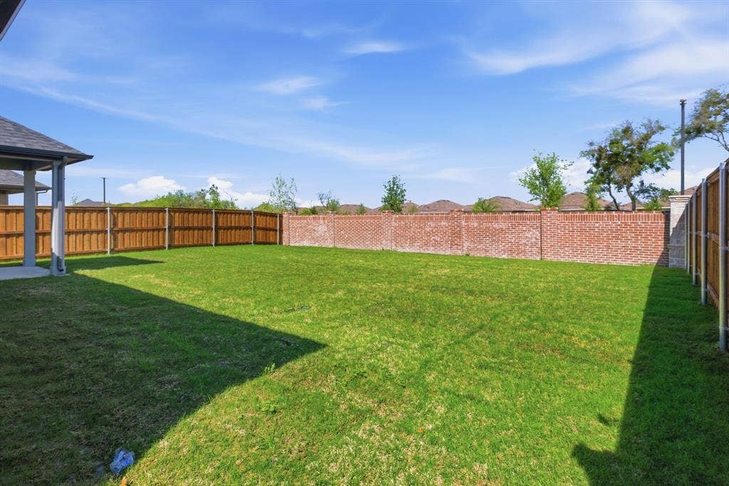 637 Sierra Ridge, Lavon, TX 75166 Expansive lawn with wood privacy fencing and a brick perimeter wall, featuring a covered patio