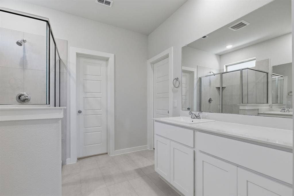 637 Sierra Ridge, Lavon, TX 75166 Frameless glass shower enclosure with tiled walls, white vanity with integrated sink and chrome faucet, large vanity mirror, and light-toned floor tile