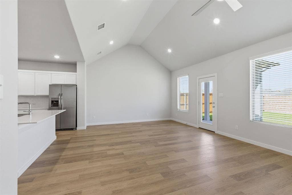 637 Sierra Ridge, Lavon, TX 75166 Vaulted ceiling with recessed lighting, wood-finish flooring, white kitchen cabinetry, stainless steel refrigerator, and a kitchen island with sink