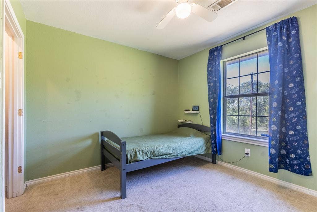 Ceiling fan with integrated lighting, window with grid panes, textured wall finish, and carpeted flooring