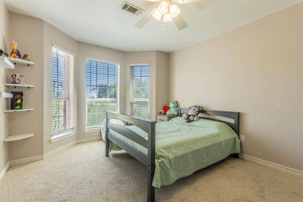 Carpeted room featuring a ceiling fan, bay window with blinds, and built-in floating corner shelves