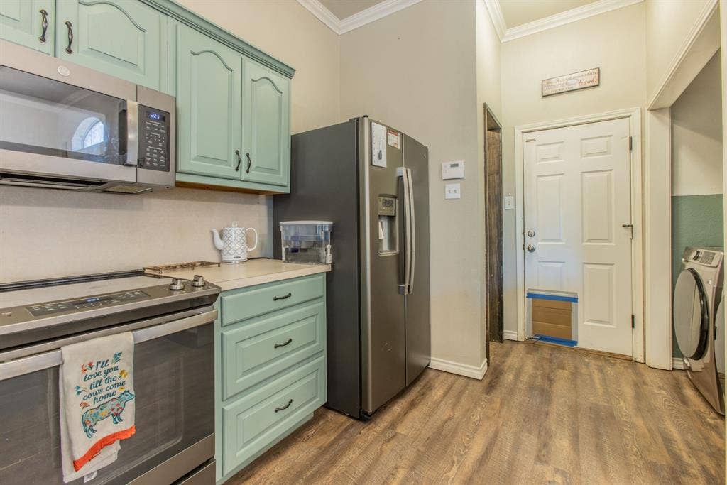 Stainless steel appliances, wood-finish flooring, light-colored countertops, and decorative cabinetry