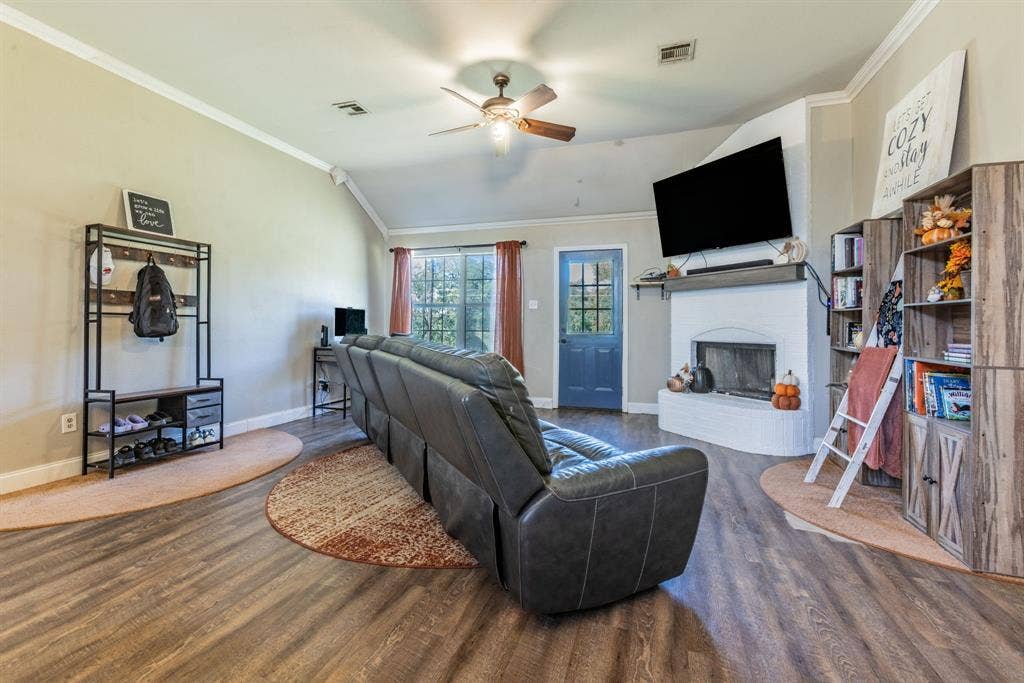 Vaulted ceiling with a ceiling fan, wood-finish flooring, white painted fireplace with a mantel, and a blue painted door with window panes