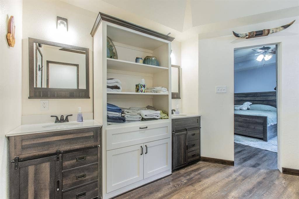 Dual wood-finish vanities with undermount sinks, built-in shelving, white countertops, and wood-finish flooring