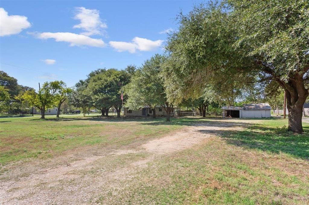 204 Ausborn Street, Eddy, TX 76524 Expansive grassy lot featuring mature trees, a gravel driveway, and a detached outbuilding
