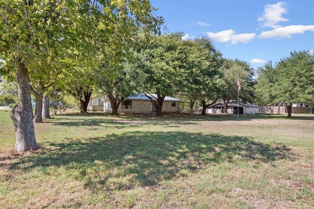 204 Ausborn Street, Eddy, TX 76524 Expansive lawn with mature trees, a single-story residence with a stone exterior, and a detached structure
