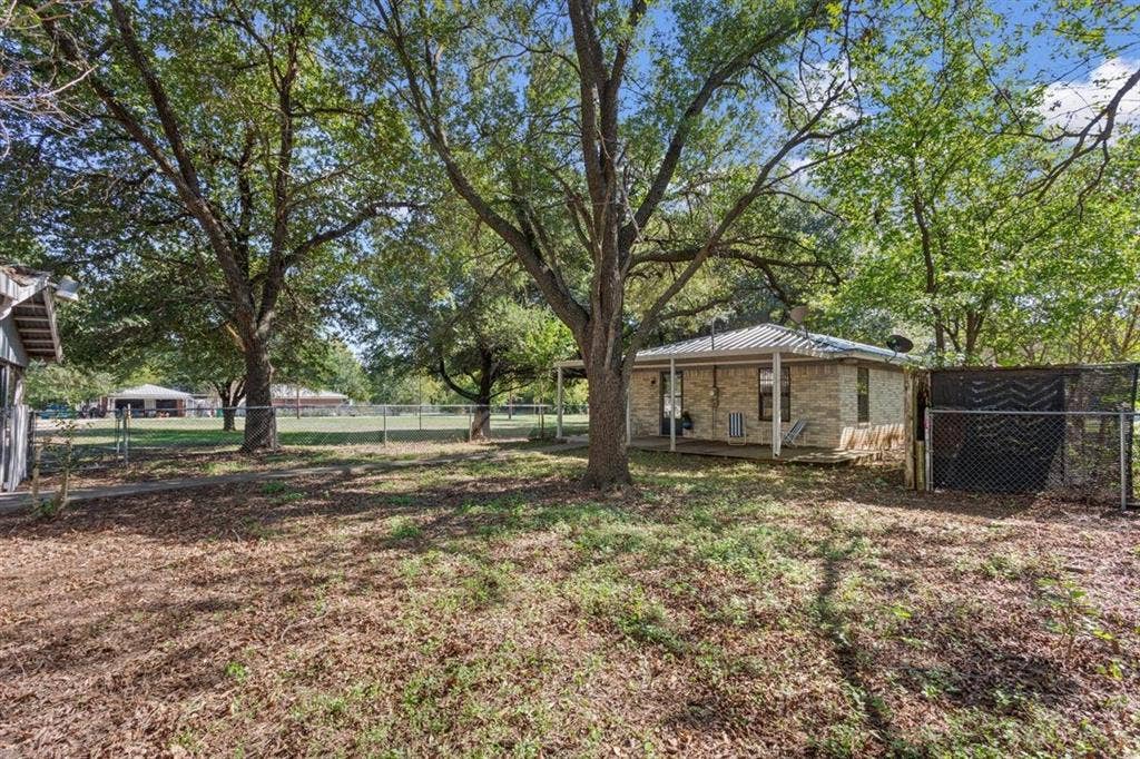 204 Ausborn Street, Eddy, TX 76524 Expansive outdoor space featuring mature trees, a chain-link fence, and a brick-sided structure with a covered porch