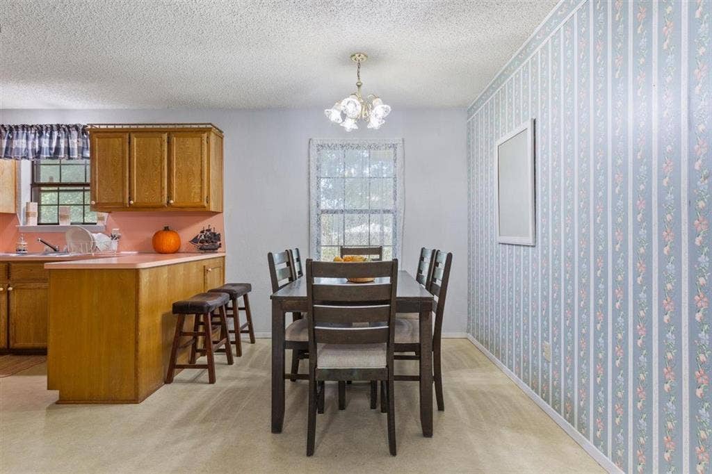 204 Ausborn Street, Eddy, TX 76524 Kitchen cabinetry with a breakfast bar, patterned wallpaper accent wall, and a dining area with overhead lighting