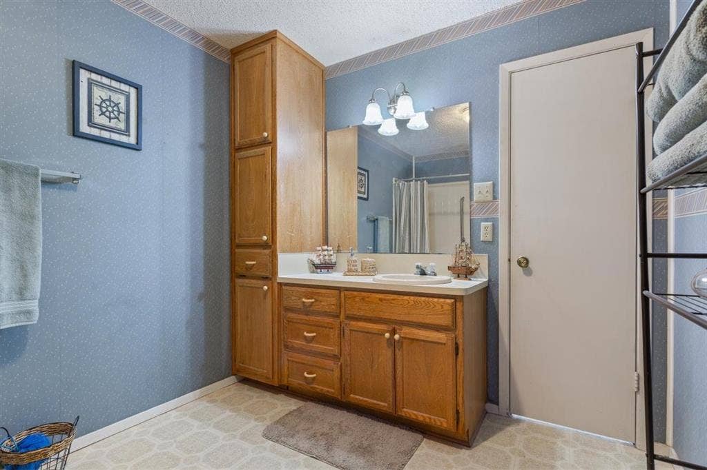 204 Ausborn Street, Eddy, TX 76524 Extended height wood-finish cabinetry, wood-finish vanity with drawer and cabinet storage, single basin sink, wall-mounted vanity mirror, and overhead sconce lighting