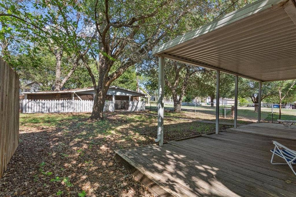 204 Ausborn Street, Eddy, TX 76524 Expansive backyard featuring a covered wood-deck patio, mature trees, a wooden privacy fence, and a white picket fence