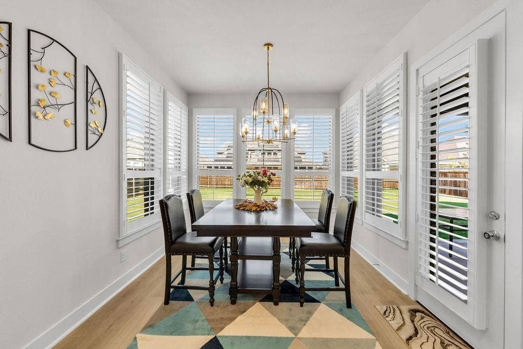 2971 Gaulding Drive, Prosper, TX 75078 Dining area featuring wood-finish flooring, multiple windows with white plantation shutters, a glass-paned door with white plantation shutters, and a linear chandelier