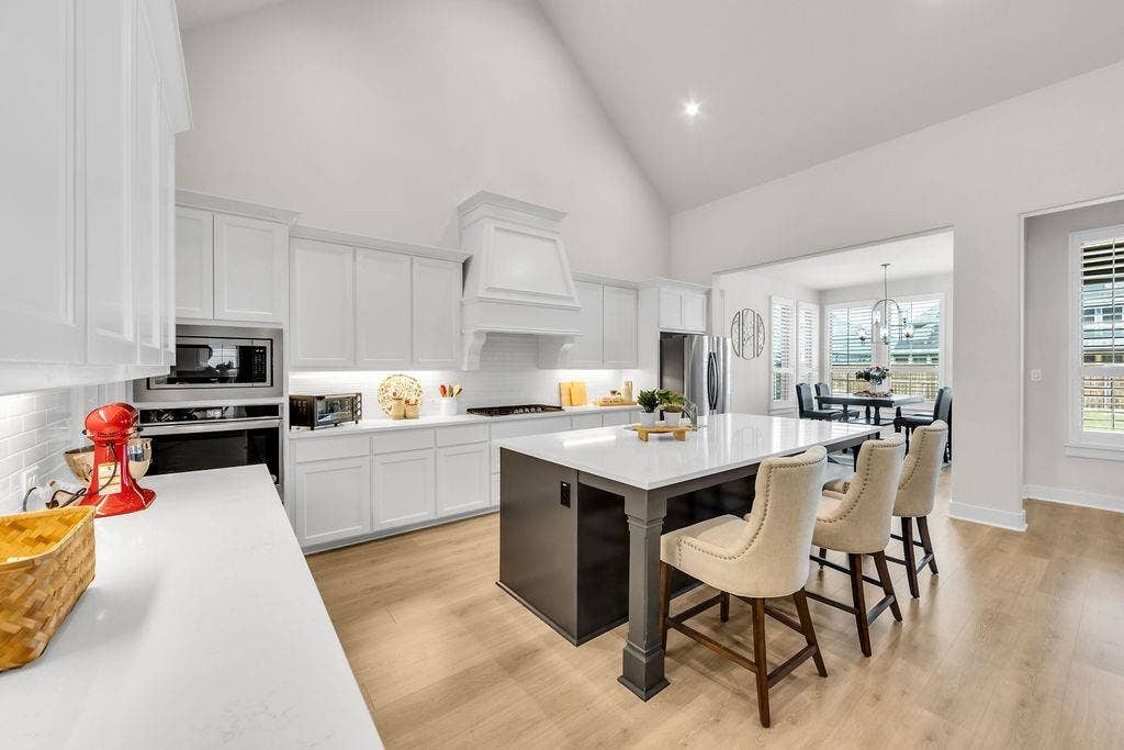 2971 Gaulding Drive, Prosper, TX 75078 Gourmet kitchen with vaulted ceiling, white cabinetry, integrated stainless steel appliances, a large center island with counter seating, and wood-finish flooring