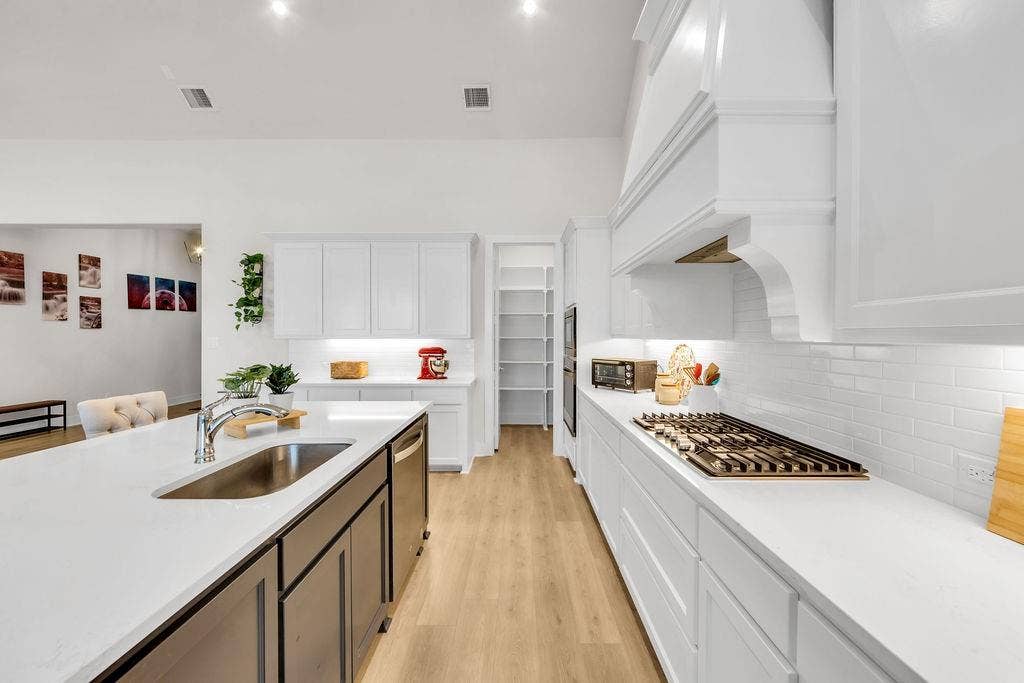 2971 Gaulding Drive, Prosper, TX 75078 Spacious kitchen featuring an expansive island with an undermount sink, white shaker cabinetry, light wood-finish flooring, and a gas range with a decorative range hood