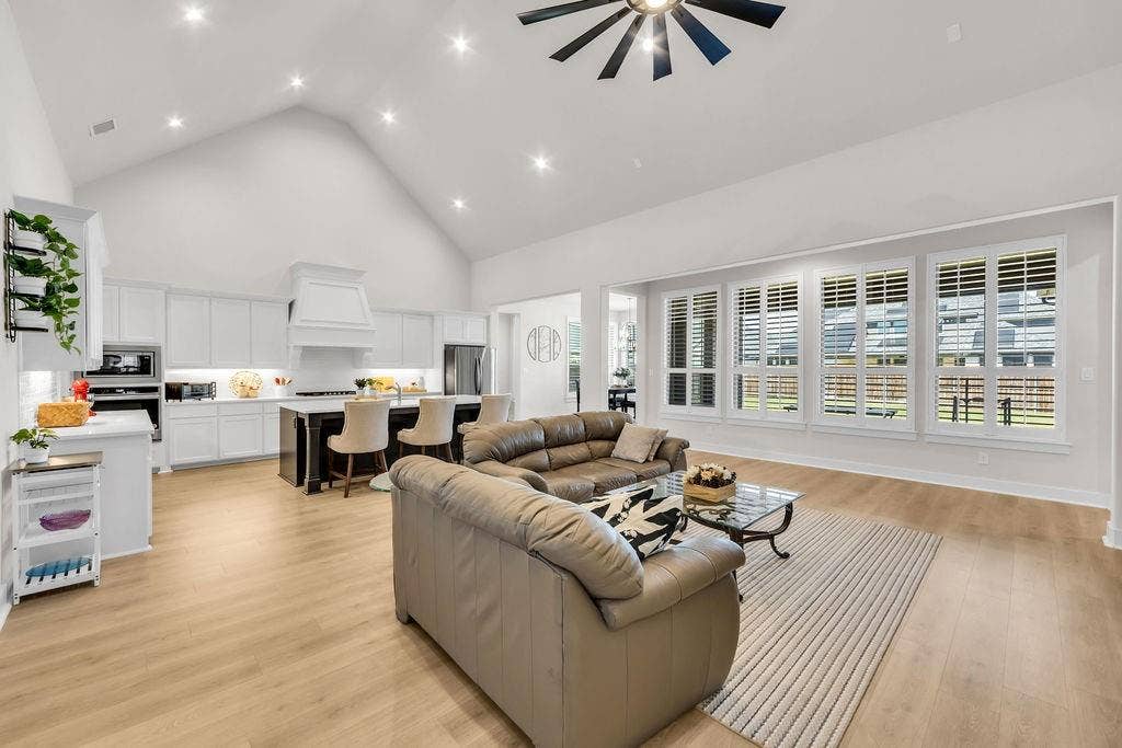 2971 Gaulding Drive, Prosper, TX 75078 Vaulted ceiling with recessed lighting and a ceiling fan, wood-finish flooring, white kitchen cabinetry, a kitchen island, and multiple windows with plantation shutters