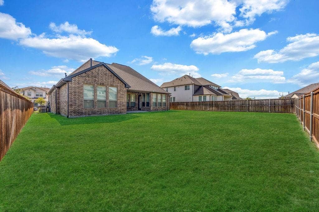 2971 Gaulding Drive, Prosper, TX 75078 Expansive backyard featuring a manicured lawn, full wood fencing, and a brick exterior home with a covered patio