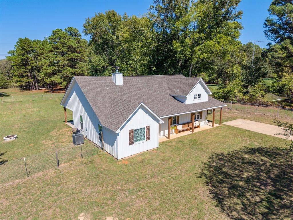 19731 County Road 4130, Lindale, TX 75771 White board and batten siding, dark shingle roof, covered front porch with wood columns, dormer window, and a gravel driveway