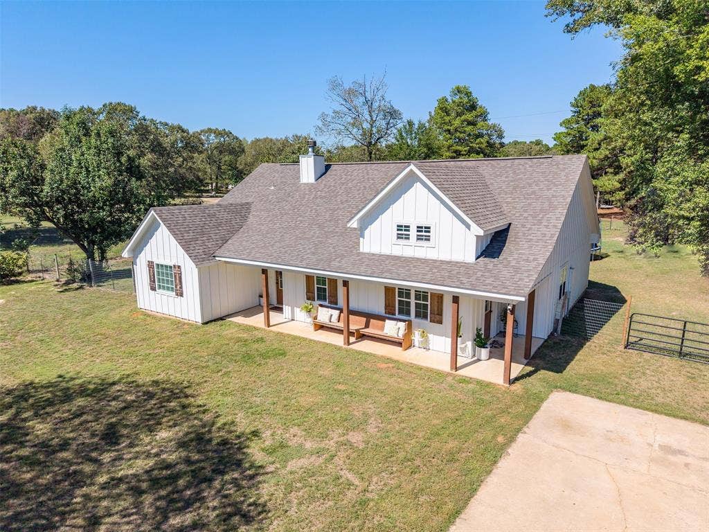 19731 County Road 4130, Lindale, TX 75771 White board and batten exterior with brown shutters, a covered front porch featuring wood-tone columns, and a dormer window
