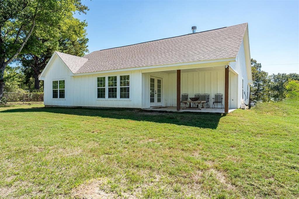 19731 County Road 4130, Lindale, TX 75771 White board and batten siding, multiple pane windows, double French doors, covered patio with wood support beams, and a gabled roof