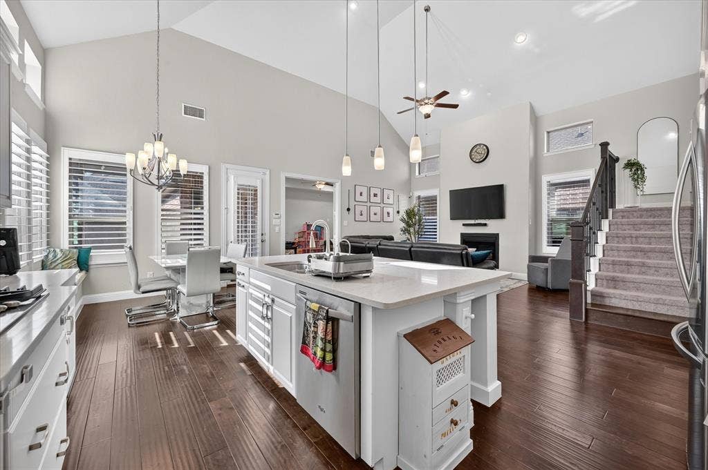 1416 White Squall Trail, Arlington, TX 76005 Open-concept living area featuring vaulted ceilings, wood-finish flooring, a kitchen island with stone countertops, a fireplace, and a staircase with carpeted treads