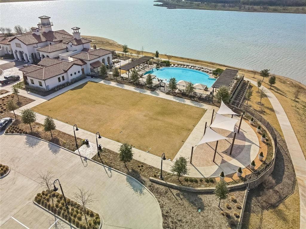 1416 White Squall Trail, Arlington, TX 76005 Waterfront property featuring a large resort-style pool, expansive green space, shaded outdoor seating, and a multi-level clubhouse with a tile roof