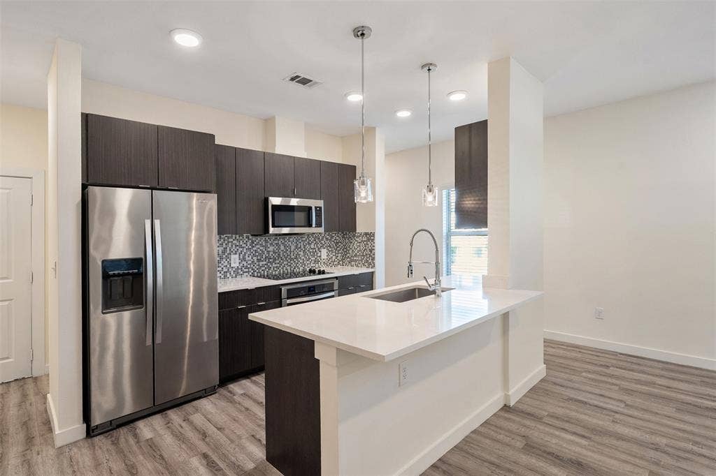 Kitchen featuring stainless steel appliances, dark wood-finish cabinetry, a patterned tile backsplash, white countertops, and wood-finish flooring