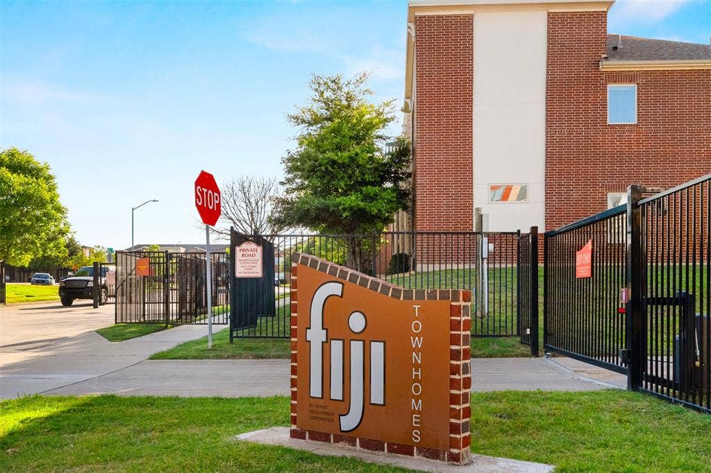 Brick facade townhome with a private gated entry, modern community signage, and manicured landscaping