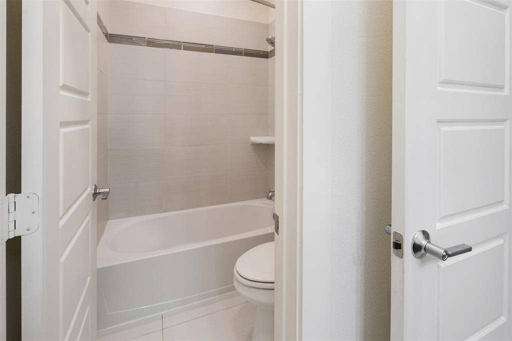 Full bathroom with a white bathtub, light-colored wall tiles, a decorative tile accent band, and a built-in shower shelf