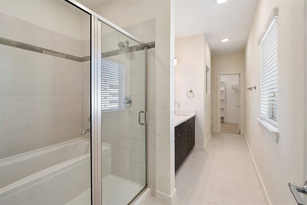 Bathroom featuring a glass-enclosed shower, bathtub, dual-sink vanity with dark cabinetry, tile flooring, and recessed lighting