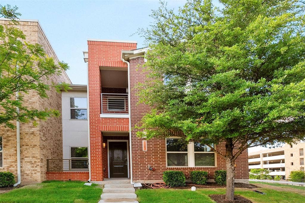 Brick facade with contemporary accents, second-story balcony with metal railing, and a ground-level covered entry