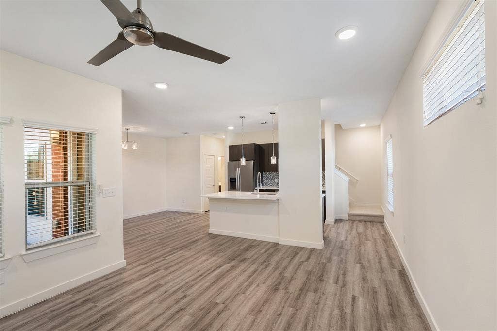Spacious open-concept living area featuring wood-finish flooring, recessed lighting, a modern ceiling fan, and a kitchen island with pendant lighting