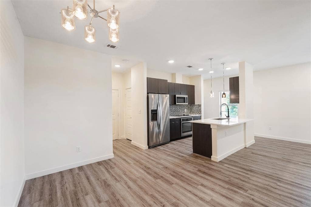 Open-concept living space with wood-finish flooring, modern kitchen, stainless steel appliances, and an island with pendant lighting