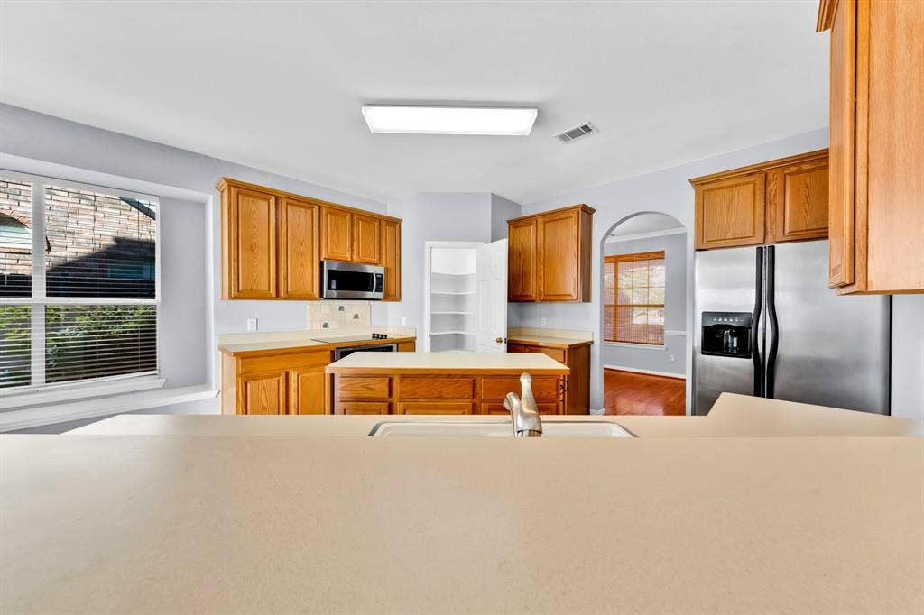 Kitchen featuring wood cabinetry, stainless steel appliances, a central island, a built-in microwave, and light-toned countertops