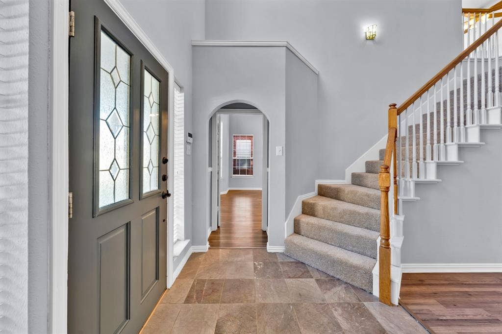 Entryway featuring a decorative glass front door, large format tile flooring, staircase with carpeted treads and wood handrails, and an arched hallway opening