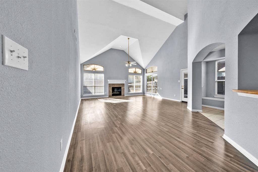 Vaulted ceiling, wood-finish flooring, fireplace with mantel, arched entryway, and multiple large windows