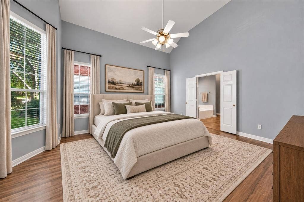 Vaulted ceiling with a ceiling fan, wood-finish flooring, multiple windows, and double doors opening to an adjoining room