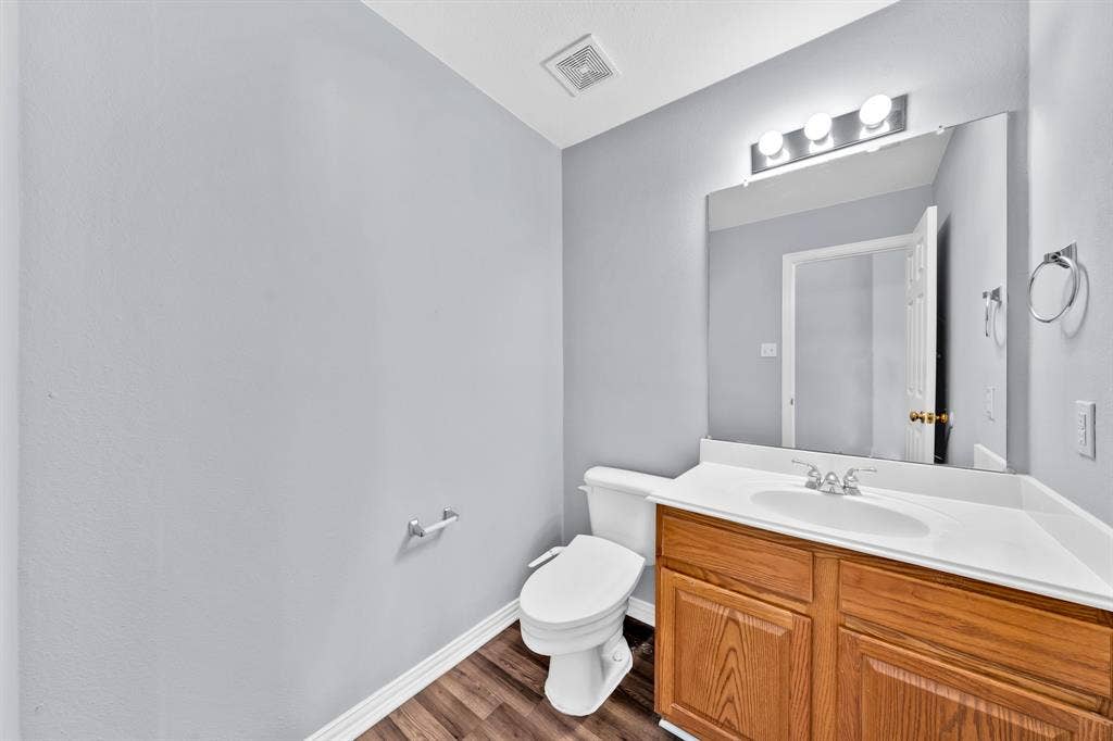 Modern bathroom featuring a wood-finish vanity with dual sink setup, white quartz countertop, large framed mirror with integrated lighting, and wood-finish flooring throughout